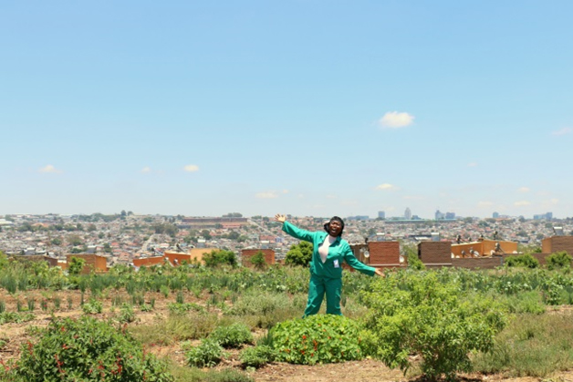 Mam Vi in her garden in Alexandra with the township of Alexandra behind her and the Sandton skyline on the horizon